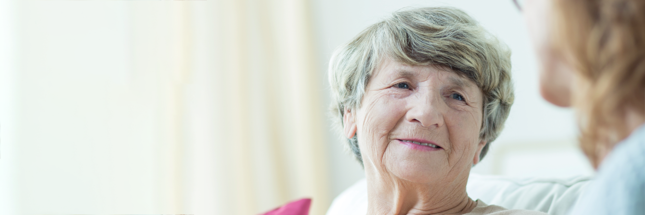 Elderly woman smiling in conversation with another woman. 